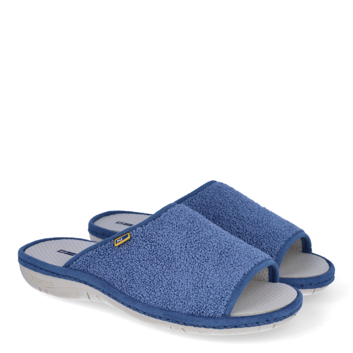 Zapatillas de casa de la marca Nordikas, modelo KAYA. Exterior de las zapatillas en toala color azul. Interior de las zapatillas en piel troquelada color blanco. Zapatilla con suela plana. Estas zapatillas Nordikas KAYA son el complemento perfecto que garantiza comodidad y ligereza al estar por casa.