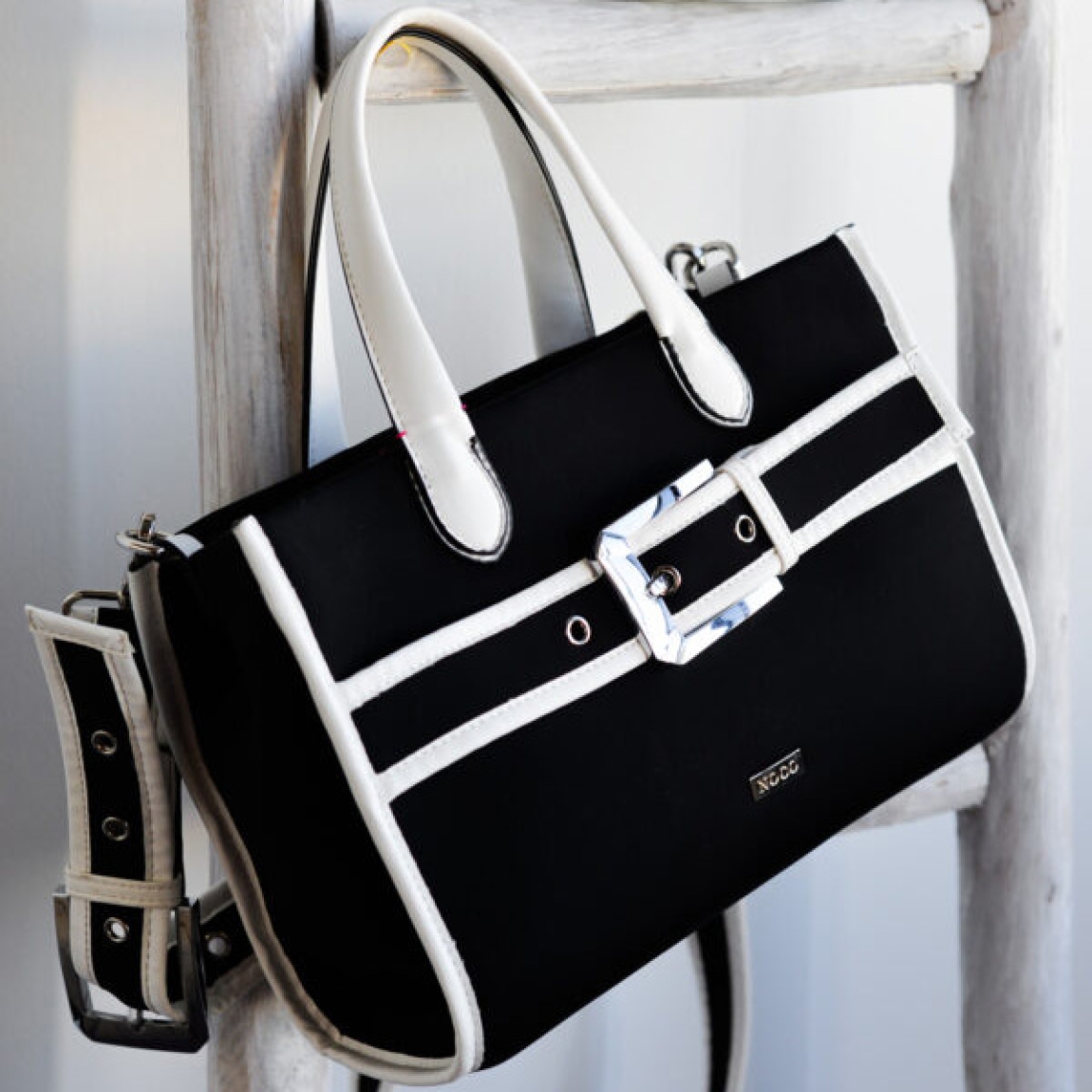 Bolso clásico de la marca Noco, modelo TORI. Elaborado en neopreno color negro con detalle en blanco. Hebilla en parte frontal del bolso. Cierre con cremallera y tiene dos asas para llevar de mano y una larga regulable. Medidas: alto 20cm y ancho 28cm. Este bolso Noco TORI tiene el tamaño mediano perfecto para quienes necesitan un bolso espacioso pero no demasiado grande. Bolso ligero y resistente.