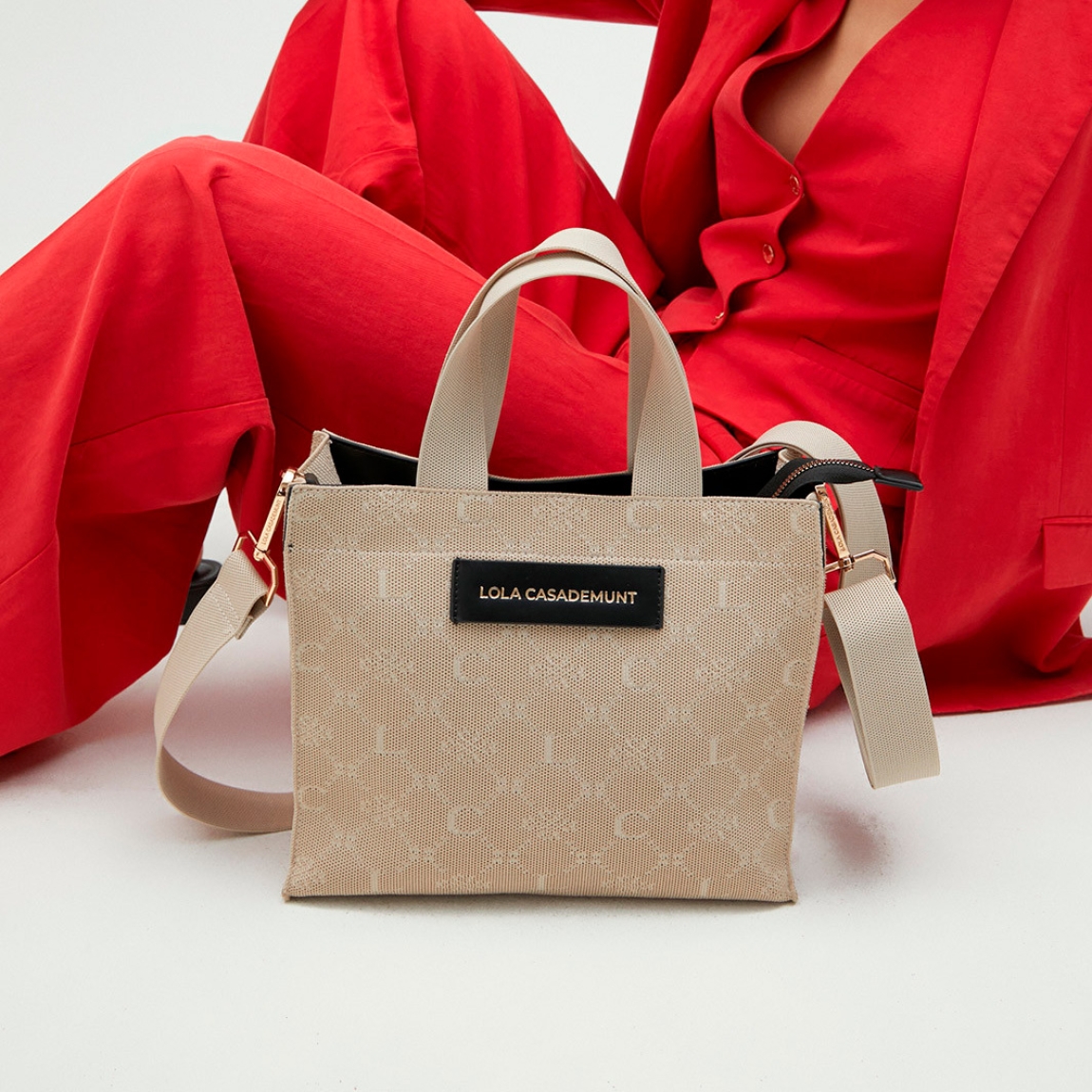 Bolso de la marca Lola Casademunt, modelo REBE. Exterior elaborado en textil color beig con estampado de logo. Interior en textil beig con amplios compartimentos. Bolso Lola Casademunt con cierre de cremallera y asas dobles, una fija de mano y otra, extraíble para mayor versatilidad de uso. Medidas: alto 24cm y ancho 28cm. Este bolso Lola Casademunt REBE es ideal para llevar a todos lados, un bolso clásico que debes tener en tu armario!