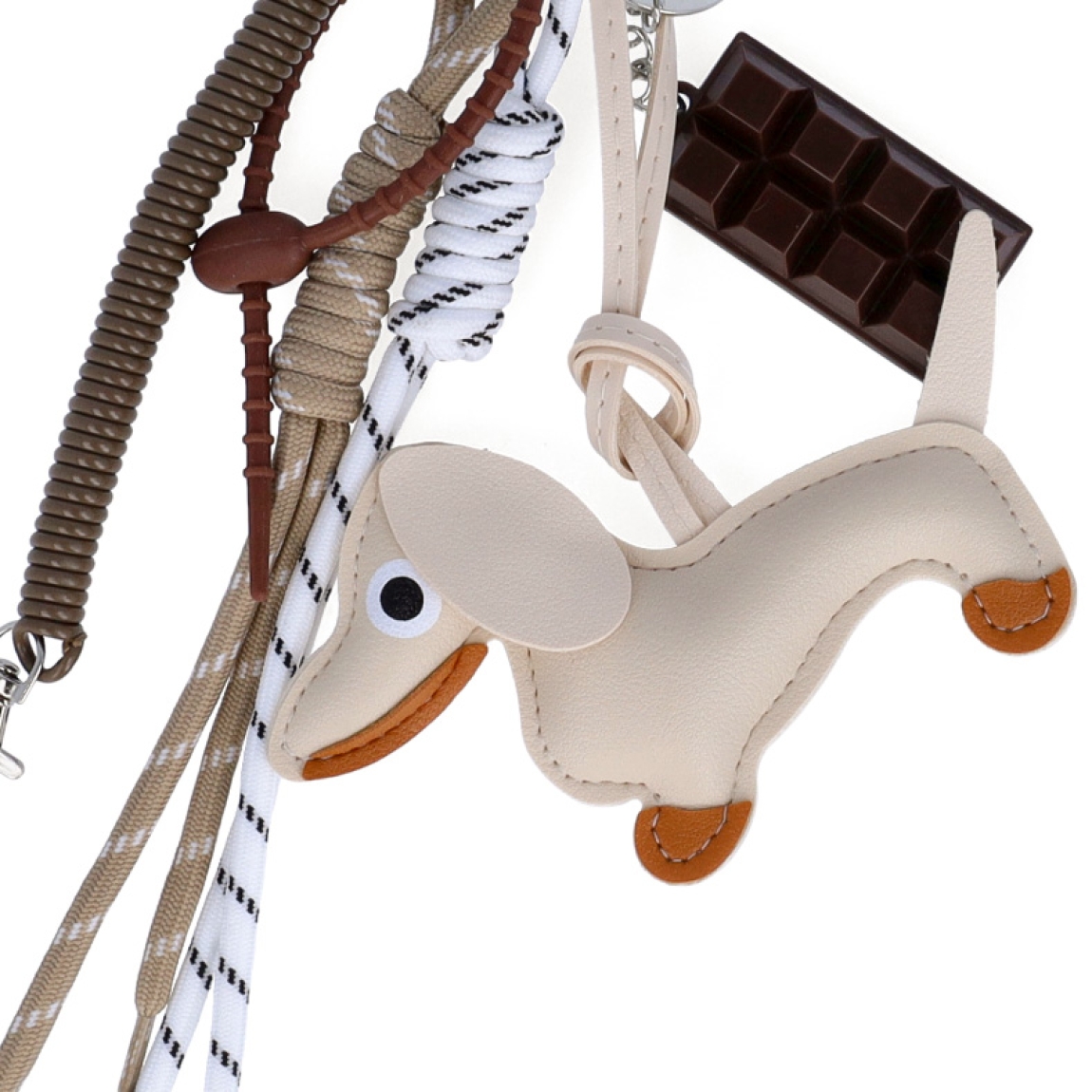Llavero de la marca MUNNÉ, modelo DOG. Elaborado en piel color beig con dijes de chocolate y perro salchicha. Complemento perfecto para tu bolso.