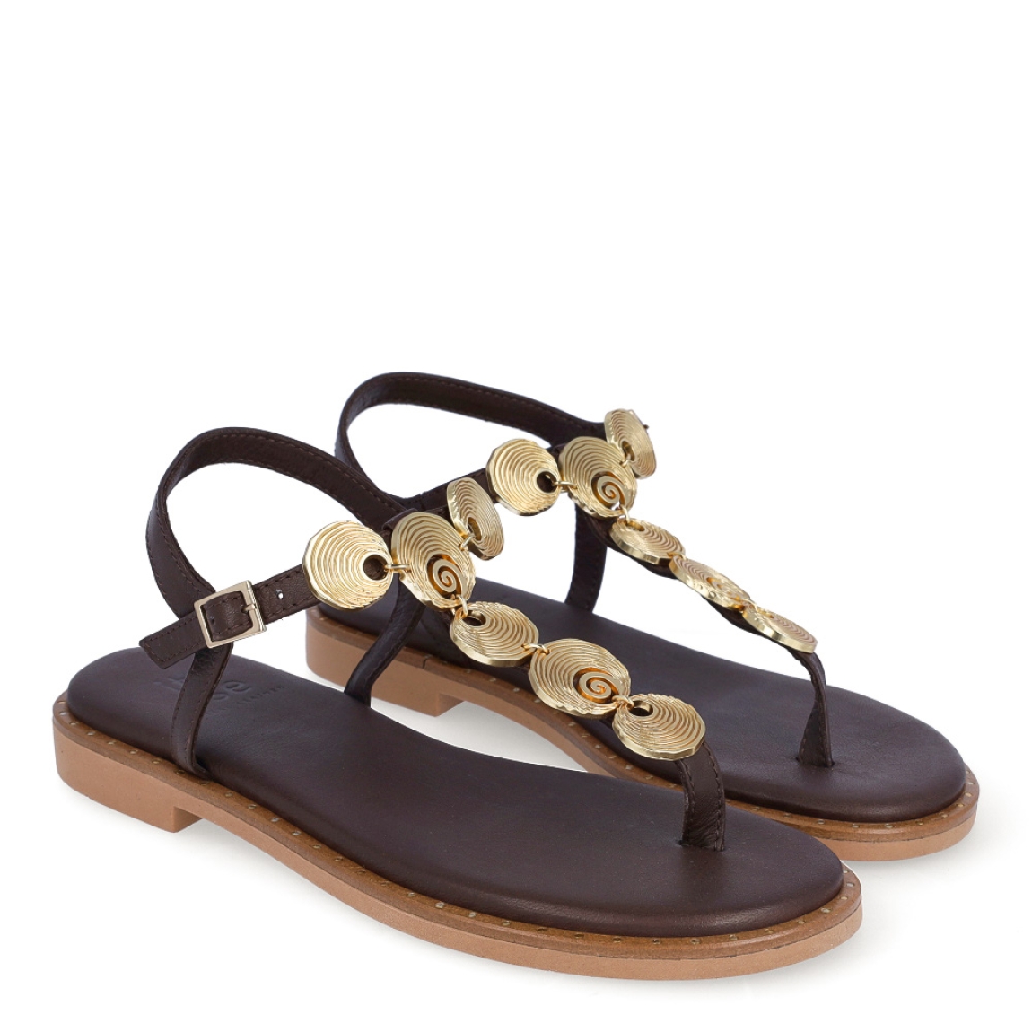 Sandalias de la marca Itse, modelo TOSCANA. Sandalias elaboradas en piel color marrón con detalles de adornos metálicos dorados en formas circulares en la pala. Cierre de las sandalias con hebilla en el tobillo y plataforma plana con detalle de tachuelas doradas. Estas sandalias Itse TOSCANA son el complemento que dará personalidad y comodidad a tus looks de temporada.