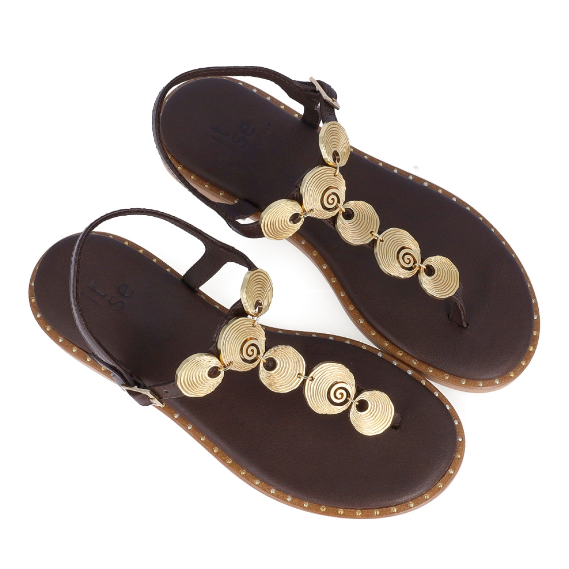 Sandalias de la marca Itse, modelo TOSCANA. Sandalias elaboradas en piel color marrón con detalles de adornos metálicos dorados en formas circulares en la pala. Cierre de las sandalias con hebilla en el tobillo y plataforma plana con detalle de tachuelas doradas. Estas sandalias Itse TOSCANA son el complemento que dará personalidad y comodidad a tus looks de temporada.
