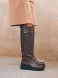Botas altas de la marca Itse, modelo BALMA. Botas elaboradas en piel color taupe oscuro con hebilla y tachuelas en parte alta exterior. Botas sin cierre y con una punta redonda. Botas Itse con plataforma de 3cm de altura, que da una comodidad en cada paso. Botas Itse BALMA con un estilo moderno y contemporáneo, perfecto para usarlo con diferentes looks.